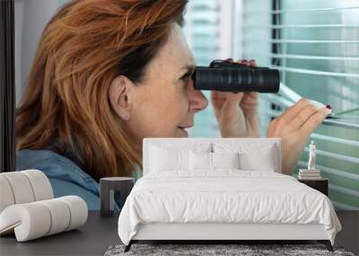 woman searches with binoculars out a window with venetian blinds Wall mural