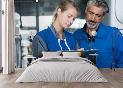 woman wearing overalls writing on clipboard supervisor watching over shoulder Wall mural