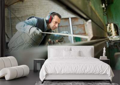 worker passing sheet metal through industrial machine Wall mural