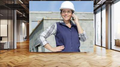 worried female contractor wearing hard hat on site using phone Wall mural