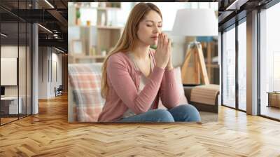 young beautiful woman at home praying with hands together Wall mural