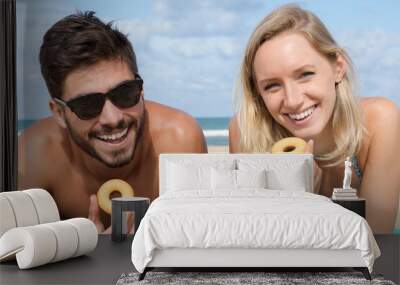 young couple on the beach eating doughnuts Wall mural