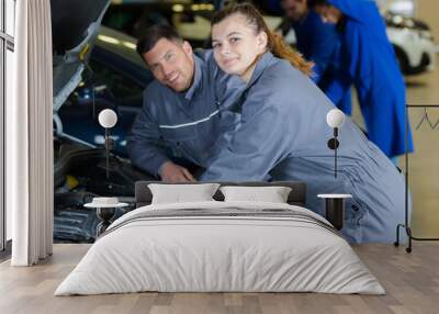 young female trainee fixing car engine in garage Wall mural