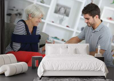 Young man getting tablets for lady with her arm in a sling Wall mural