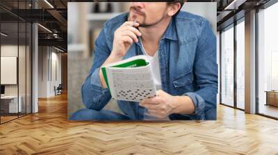 young man sitting doing a crossword puzzle looking thoughtfully Wall mural