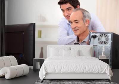 Young man teaching an elderly man computer skills Wall mural