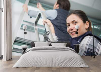 young smiling woman helping colleague on a ladder Wall mural