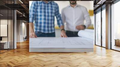 Close-up of two professionals discussing architectural plans on a table, showcasing teamwork and project collaboration. Wall mural