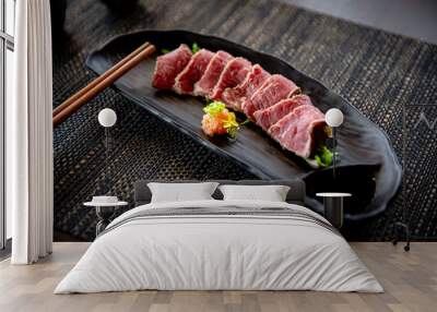 Beef tataki appetizer in the traditional Japanese ramen restaurant, with a black plate on a black mat in a black scene background Wall mural