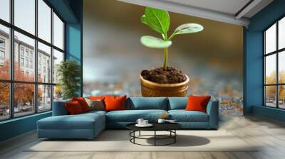 A small plant is growing in a small pot. The pot is made of metal and has a leaf design. The plant is surrounded by dirt and he is thriving Wall mural