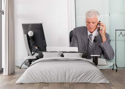 senior businessman using a cell phone and writing an information on a document in his office Wall mural