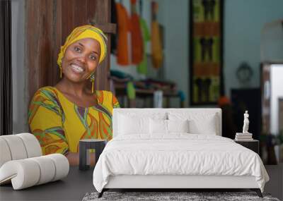 Smiling black African woman in traditional clothes wishing welcome to customers in front of her store Wall mural