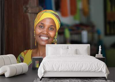 Young African woman in traditional clothes standing in entrance of her store, smiling at camera Wall mural