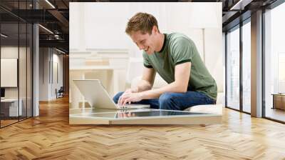 man sitting on sofa in livingroom typing on laptop Wall mural