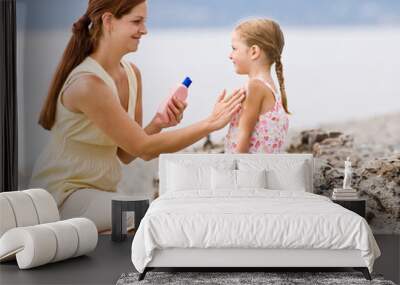 Mother applying sunscreen to daughter at beach Wall mural