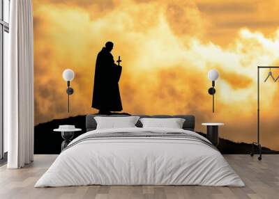 Silhouette of priest holding cross at sunset, religious figure on hill with dramatic sky, spiritual solitude and faith, Christianity, catholic Wall mural