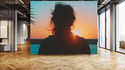 Silhouette of woman seen from back while she is watching sun rising in tropical country, evening, dusk or dawn Wall mural