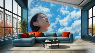 Young asian woman looking up with closed eyes, blue sky with clouds on the background, happy life Wall mural