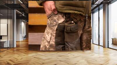 Photo of a soldier in a green-brown tactical body armor, military uniform and gloves, standing against a background of brown wood.close-up, front view. Wall mural