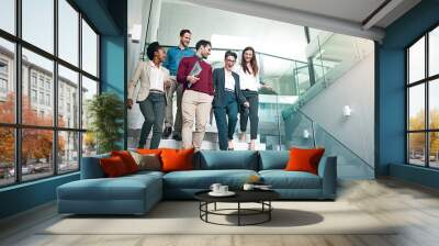 The end of another successful business day. Shot of a group of colleagues talking together while walking down stairs in a large modern office. Wall mural