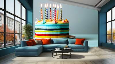 A vibrant striped birthday cake with lit candles on a light blue background, space for your message. Birthday concept theme. Wall mural