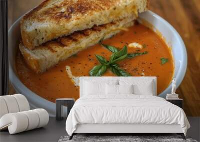 A bowl of creamy tomato soup, garnished with a swirl of cream and a sprinkle of fresh basil, perfect for dipping a grilled cheese sandwich. Wall mural