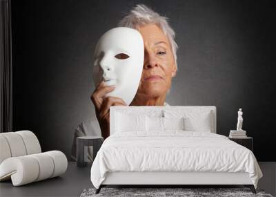 serious looking older woman revealing true face behind mask Wall mural