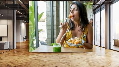 Candid lifestyle portrait of fashionable healthy ethnic businesswoman eating an organic vegetarian cauliflower dish for vegans and drinking green smoothie Wall mural