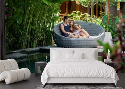 Candid shot of young caucasian couple lounging in modern chair near luxurious pool of tropical hotel and spa in Bali Wall mural