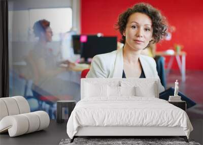 Confident female designer working on a digital tablet in red creative office space Wall mural