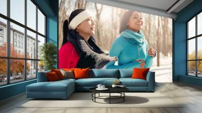 Multi-ethnic pair of female friends taking a break from jogging in the snow in winter Wall mural