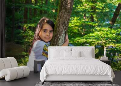 Little girl hugging a tree in the forest and smiling towards the camera Wall mural