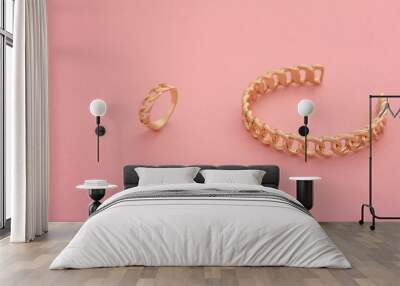 Top view of chain shape golden bracelet and ring on pink background Wall mural