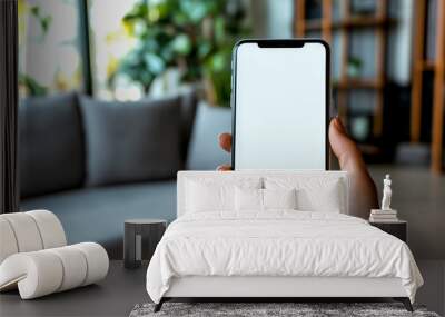 Close-up of a woman's hands using a black smartphone with a blank screen against a blurred living room. Wall mural