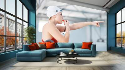 Swimming pool, lifeguard and woman blowing whistle with goggles for safety training exercise at club. Professional water sports, life saving workout and swimmer at swim competition with attention Wall mural