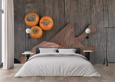 Male cuts persimmon fruit into two pieces on wooden surface Wall mural