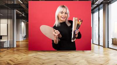 Young artist woman holding art supplies on a red background Wall mural