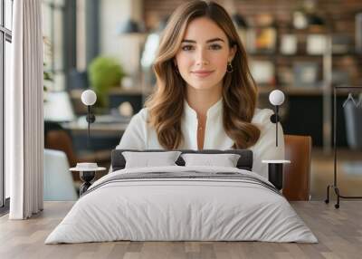 A smiling businesswoman in a white shirt sits at a desk in an office. Wall mural