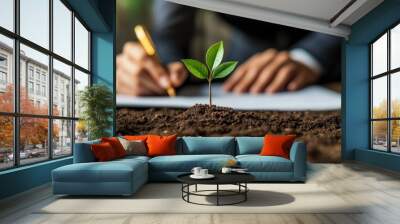 Small green plant growing out of the ground in front of a person signing a document. Wall mural