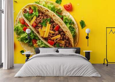 Two delicious tacos with ground beef, lettuce, cheese, and tomatoes on a bright yellow background. Wall mural