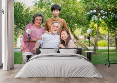 Senior man with his family in park. Chinese old man in wheel chair and his senior chinese wife, grand son and daughter relaxing together, talking to each other. Family insurance concept. Wall mural