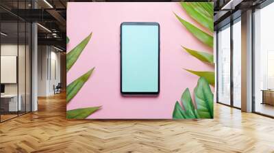 A smartphone placed on a pink backdrop surrounded by green leaves for a fresh and modern look in a creative setting Wall mural