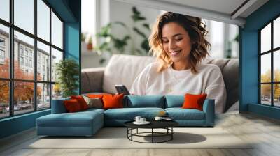 A smiling girl is sitting on the sofa with a phone in her hands. Wall mural