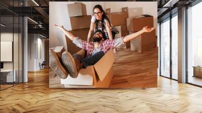 	 Young couple moving into a new home.Man sitting in cardboard box while woman pushes him all over the room.Real estate funny concept.	 Wall mural