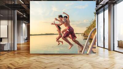 A group of young people joyfully jump into the refreshing lake waters on a sunny summer day, embracing the carefree moments of pure fun and laughter. Wall mural