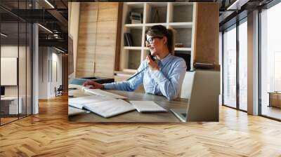 Businesswoman in her office.She sitting at the desk and talking on the phone. Wall mural