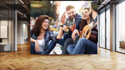 Group of young people hangout  on street in downtown.They standing by the city square,drinking and playing guitar. Wall mural