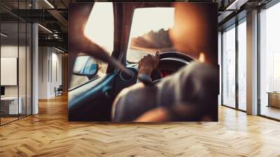 Man driving car, hand on steering wheel, looking at the road ahead,sunset. Wall mural