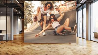 Two female friends playing with skateboard at the skate park.One girl pushing other from behind.Laughing and fun. Wall mural