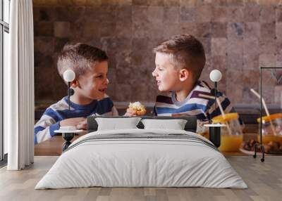 Two little boys eating sweet vanilla cakes at the kitchen. Wall mural